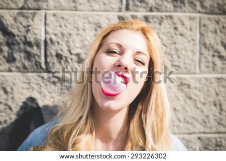 Young beautiful caucasian blonde girl playing with bubblegum in the city having fun - emancipation, relax, freedom concept