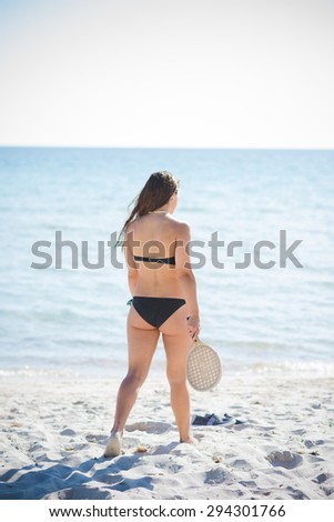 young beautiful back brunette woman wearing swimsuit in summertime at the beach playing on the foreshore with racket  - sport, relax, fun concept