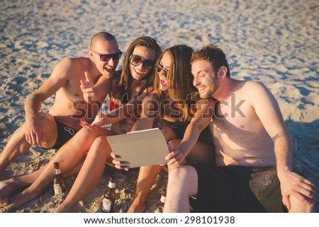 Group of young multiethnic friends with digital tablet sitting at the beach taking a selfie -  multicultural friendship and social media networking concepts - Interacting with technological devices
