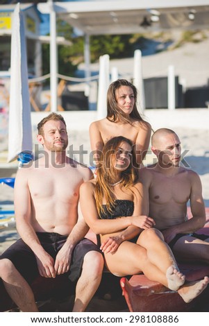Group of young multiethnic friends seated on paddle boat in swimsuit looking at the horizon at the beach at sunset - future, relax, friendship concept