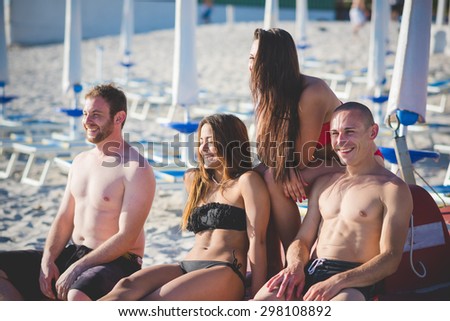 Group of young multiethnic friends seated on paddle boat in swimsuit looking at the horizon at the beach at sunset - future, relax, friendship concept