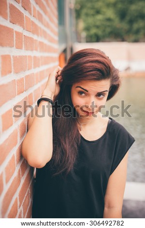 Half length of a young beautiful reddish brown hair caucasian girl posing leaning against a wall looking in camera - carefreeness, freshness, youth concept - dressed blue jeans and black shirt