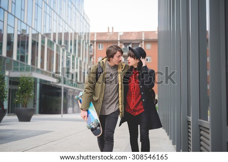 Couple of beautiful woman and man, with moustache and skate,walking through the streets of the city hugging and chatting- freshness, youth, carefreeness concept