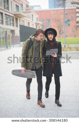 Couple of young beautiful woman and man, with moustache and skate, walking through the city using a tablet - technology, social network, communication concept