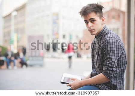 Half length of a young alternative handsome man with central labret and nostril piercing seated using a tablet connected online - social network, communication, technology concept