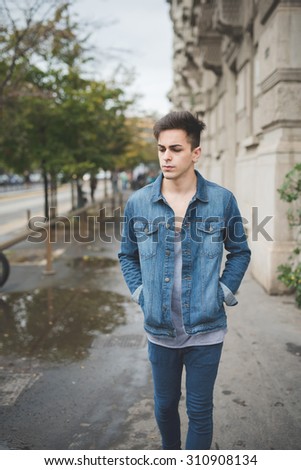 Knee figure of a young handsome caucasian dark model walking looking right with central labret and nostril piercing and hands in pocket - rebellion, youth, diversity concept
