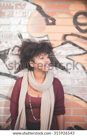 half length of a beautiful black curly hair african woman leaning against a wall in town, overlooking left, smiling - youth, carefreeness, relaxing concept