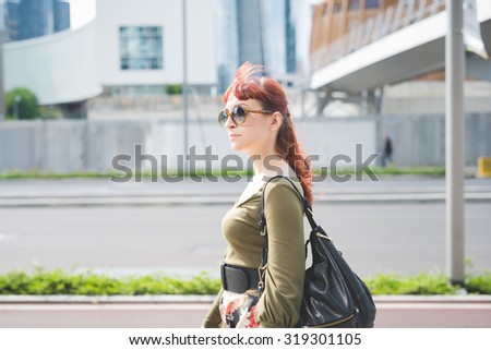 Half length profile of a young handsome caucasian redhead woman, walking in the city, overlooking left, pensive - seriousness concept - wearing floral skirt, green shirt, bag and sunglasses