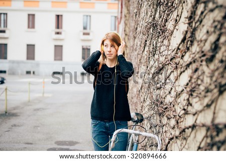 Knee figure of young beautiful hipster sporty blonde woman with her bike, wearing her headphones, overlooking right - music, sportive concept - wearing black shirt and blue jeans