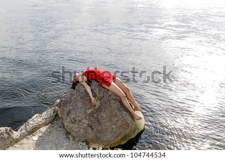 Young woman in red dress lying on rock at coast