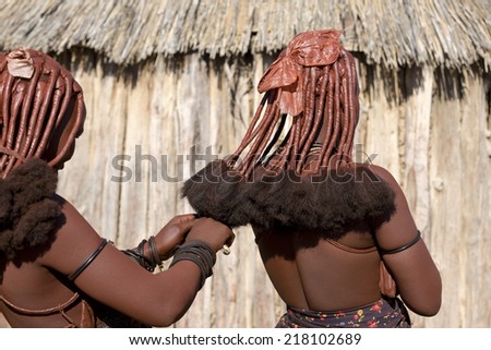 Rear view of himba women that make each other the traditional hairstyle of Himba