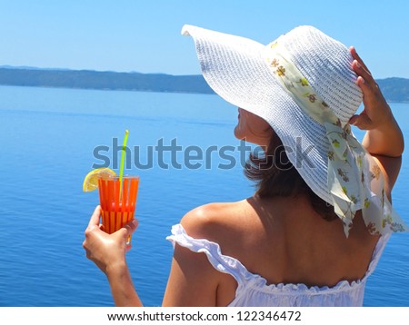 Beautiful woman drinking a cocktail by the sea,With a cocktail at Sea,photography.Natural daylight into the shadows of the hat.The main focus of the hat, soft focus on the face.