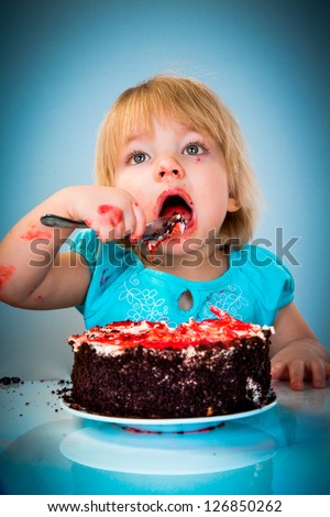 Little baby girl eating cake on a blue background