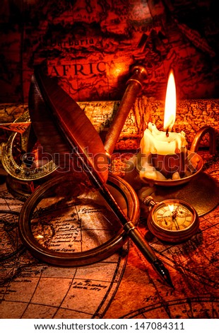 Vintage compass, magnifying glass, pocket watch, quill pen, spyglass lie on an old ancient map with a lit candle. Vintage still life.