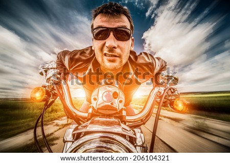 Funny Biker in sunglasses and leather jacket racing on the road with the sun in the background
