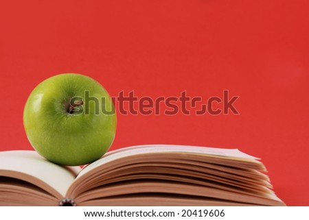 green apple and book, red background