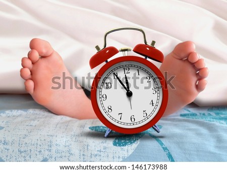 Sleeping under blanket at home with alarm clock