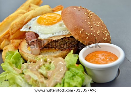 Lunch with burger, chips, eggs, sauce and salad on gray plate from stone slate