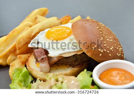 Lunch with burger, chips, eggs, sauce and salad on gray plate from stone slate