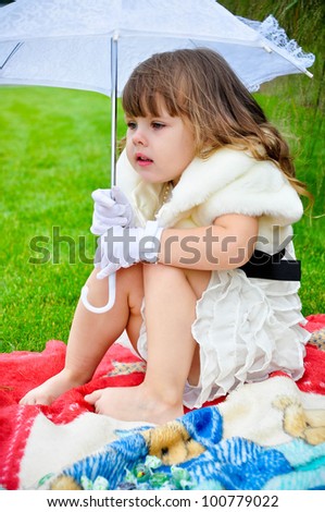 Pretty little girl is cold & hiding under umbrella in the park barefooted