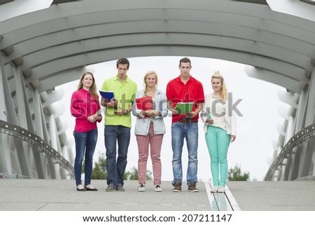 Five students standing on a bridge with their school supplies