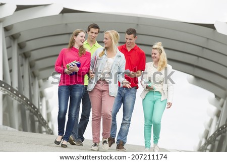 Five students walking on a bridge and they laugh with each other.