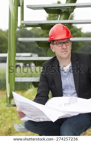 Mid adult businessman in blazer holding blueprint while looking away in storage tank park