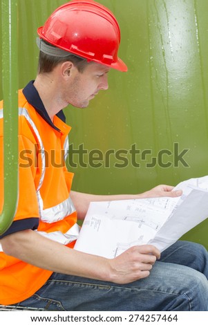 Side view of male architect analyzing blueprint while sitting in storage tank park