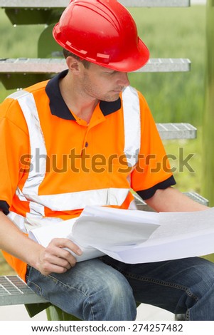 Mid adult male architect looking at blueprint while sitting on steps in storage tank park