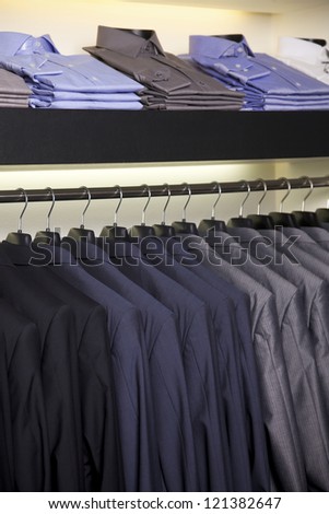Suits on hangers and dress shirts in elegant clothing store.