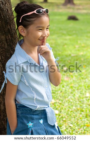 Portrait of beautiful little asian girl in the park,  she make finger on lips, Thailand.