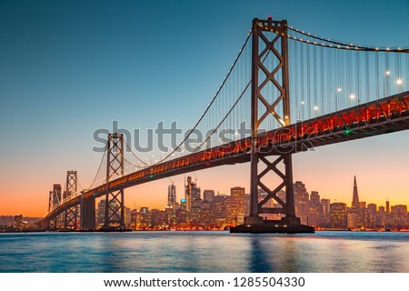 Classic panoramic view of San Francisco skyline with famous Oakland Bay Bridge illuminated in beautiful golden evening light at sunset in summer, San Francisco Bay Area, California, USA