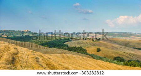 Rolling hills and harvest fields in golden evening light with famous Cappella della Madonna di Vitaleta and the old town of Pienza in the background, Val d\'Orcia, Tuscany, Italy