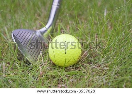 All weather yellow golf ball addressed by wedge iron and ready to be hit from the rough