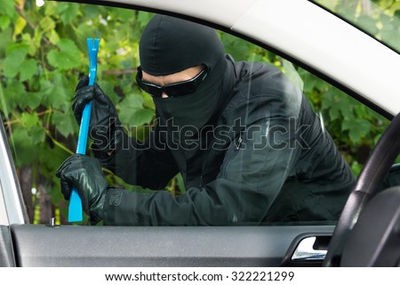 Car thief preparing to break a parking vehicle's window with special utensil.