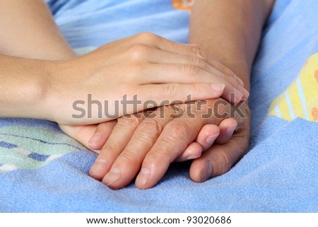Hand touches and holds an old wrinkled hand