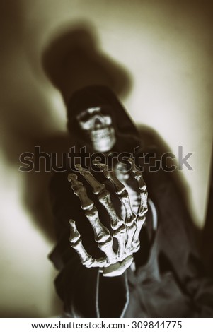 Dark Skeleton Hand Skull Blur. Skeleton in hoodie with hand reaching out as if begging or reaching for viewer. Shot with spot lighting and edited with vintage filters. Skull blurred, hand in focus.