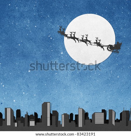 Santa Claus On Sledge With Deer And Moon above city panorama silhouettes  recycled papercraft