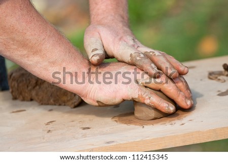 Hands of potter forming wet clay on a wooden plank