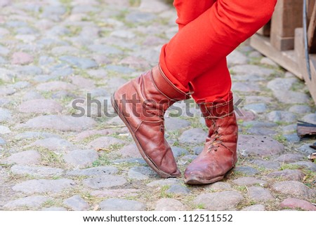 Crossed legs of a man in red pants and  middle ages boots on a carriageway