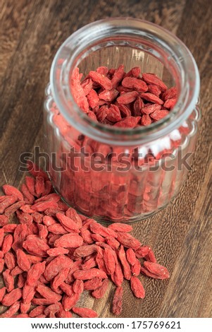 Goji berries and glass bowl closeup on brown wooden table. Shallow depth o field