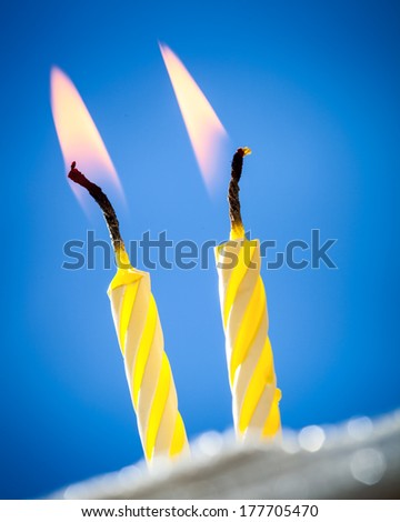 Two burning birthday candles over blue background