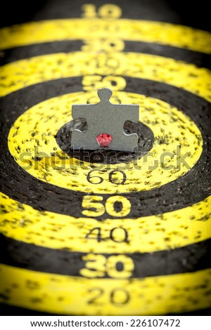Jigsaw puzzle piece in shape of a standing man in a center of old target