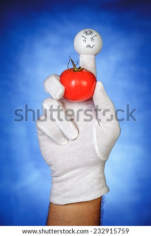 Angry finger puppet holding tomato fruit over blue background