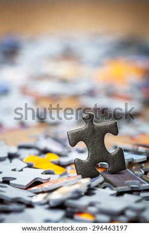 Black jigsaw puzzle piece on heap of color puzzle pieces. Shallow depth of field