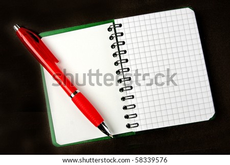 Opened notebook squared page with red pen over it on black background