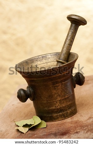 Old bronze mortar and pestle with bay leaves on yellow background