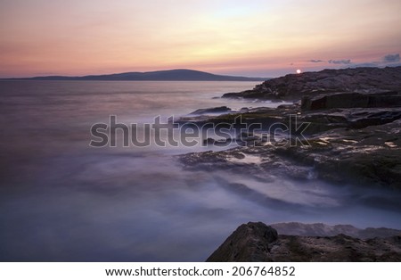 The sun sets against a rocky coast at Schoodic Point in Acadia National Park, Maine. Long exposure to achieve the misty effect of the ocean.
