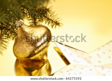 Christmas bulb, pine branch, and gold star on gold background with reflection and copy space