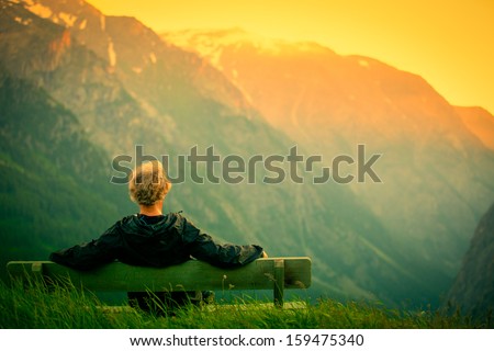 man sitting on bench in mountains